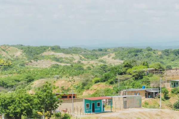 Kırsal alanda küçük bir ev ve birkaç ev daha var. Evler ağaçlarla çevrili ve gökyüzü bulutlu.