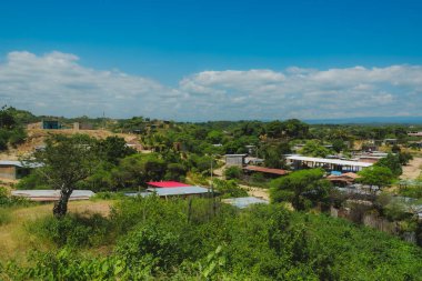 Birkaç evi ve bir ağacı olan bir kırsal bölge. Gökyüzü mavi ve bazı bulutlar var.