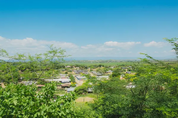 Uzakta küçük bir kasabası olan yemyeşil bir yamaç. Gökyüzü açık ve mavidir ve güneş ışıl ışıl parlar.