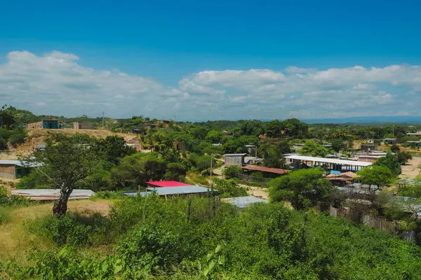 Birkaç evi ve bir ağacı olan bir kırsal bölge. Gökyüzü mavi ve bazı bulutlar var.