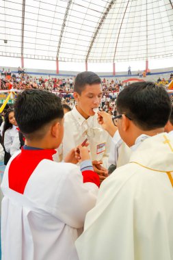 Tumbes, Tumbes, Peru 21-10-2023, Doğrulama Ayini: Beyaz cüppeli bir adam bir çocuğu besliyor. Sahne büyük bir stadyumda kalabalık bir kalabalık tarafından izleniyor.