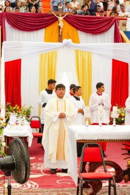 Tumbes, Tumbes, Peru 21-10-2023, Ayin Ayini: Üzerinde haç olan beyaz cüppeli bir adam masanın önünde duruyor. Odada birkaç kişi daha var, bazıları beyaz cübbe giyiyor. Oda kırmızı ve sarı c ile süslenmiş.