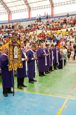 Tumbes, Tumbes, Peru 21-10-2023, Doğrulama Ayini: Mor cüppeli bir grup adam, elinde bayrak olan bir sıra bekliyor. Pankartta 
