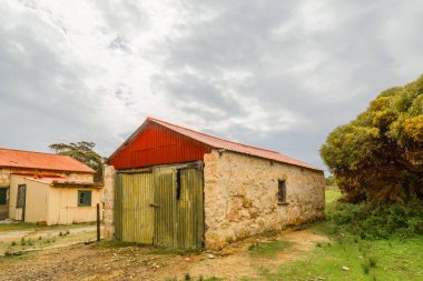 Güney Avustralya 'daki Yorke Yarımadası' nda bulutlu bir gökyüzü arka planına sahip terk edilmiş bir alçıtaşı madencilik kasabasında eskiden kırmızı cephe ve taş duvarlı tebeşir fabrikası olan eski bir taş baraka..