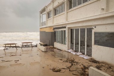 Sahilde bir bina tahtalarla kaplanmış ve kum torbasıyla kapatılmış, burada görülen, indirgenmiş bir kasırga sahile vurduktan sonra, ve bankları, vahşi sörfleri ve Avustralya 'nın Altın Sahili' ndeki bulutlu gökyüzünü gösteriyor..