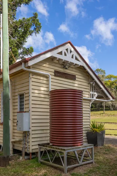 Tahta binanın bir ucunda kıvrımlı demir su tankı olan yenilenmiş bir demiryolu istasyonu ve Queensland, Avustralya 'da bulunan Imbil' de bulutlarla kaplı mavi bir gökyüzü..
