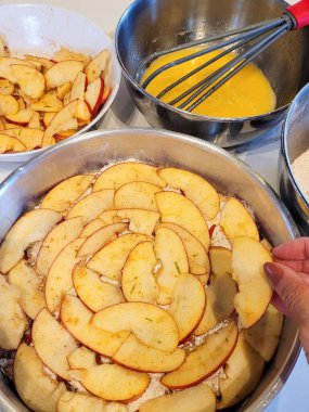Çırpılmış yumurtalar ve bir kasede gevşek elma dilimleriyle çevrili elma dilimleriyle hazırlanmış bir pasta hazırlığı. Ev yapımı pişirme sevgisini ve malzemelerin rengini iletir.