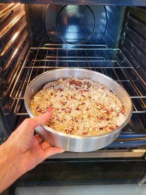 Bir el, modern bir fırının içinde pişirmeye hazır sağlıklı bir pastayla birlikte bir yemek tepsisini tutar. Pasta yulaf, fındık ve kurutulmuş meyve içeriyor, rahatlık ve beslenme hissi uyandırıyor.