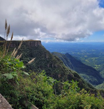 Brezilya dağlarının ağaçlarla kaplı panoramik manzarası ve parçalı bulutlu bir gökyüzünün altındaki çalılar. Manzara, görkemli uçurumlarla doğal güzellikleri resmediyor.
