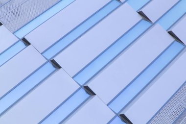 Geometrik desenleri ve yansıtıcı cam elementleri olan modern bir binanın ön cephesine yakın çekim. Soyut tasarım simetriyi, minimalizmi ve çağdaş mimariyi vurgular. Yüksek kalite fotoğraf