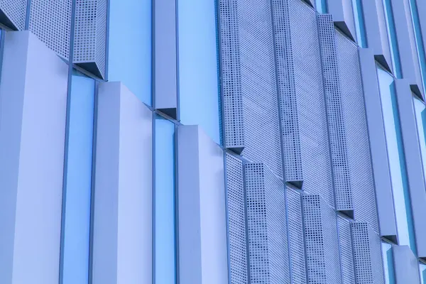 Dikey mavi cam paneller ve delinmiş metal elementlerle modern bina cephesi. Geometrik tasarım, yansımaları ve simetrisi olan soyut bir mimari model yaratır. Yüksek kalite fotoğraf