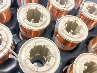 Endüstriyel bakır bobinlere yakın çekim, titizlikle silindirik çekirdeklerin etrafına sarılmış. Görüntü, modern çağda duyarlılık mühendisliği, elektrik iletkenliği ve estetik üretimi sergiliyor.