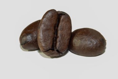 Arka planda kavrulmuş kahve çekirdeklerinin yakın plan makro fotoğrafı. Yumuşak ışıklandırma, onların şekillerini ve parlak yüzeyleri ile mat arkaplanı arasındaki zıtlığı vurgular..