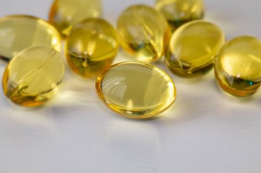 Beyaz arka planda sarı balık yağı kapsülleri. Sağlıklı yağ açısından zengin Omega-3 beslenme takviyesi. Kalp ve beyin sağlığı için besin desteği konsepti beyaz arka planda sarı balık yağı kapsülleri