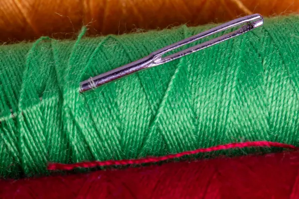 Kırmızı arka planlı yeşil iplik makarasına dikiş iğnesi yakın plan. Tekstil işçiliği araçları ve malzemelerinin makro görünümü.