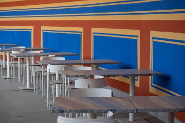 Granit masalı boş bir kafeterya ve beyaz sandalyeler kırmızı, sarı ve mavi desenli renkli geometrik bir duvara karşı..
