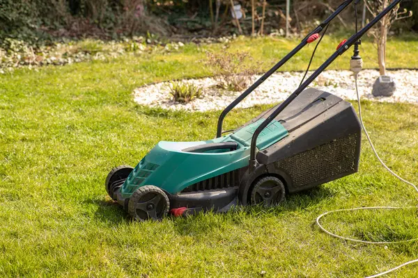 Bahçedeki yeşil çimlerin üzerinde elektrikli çim biçme makinesi. Bahar mevsiminde bahçe bakım ekipmanları.