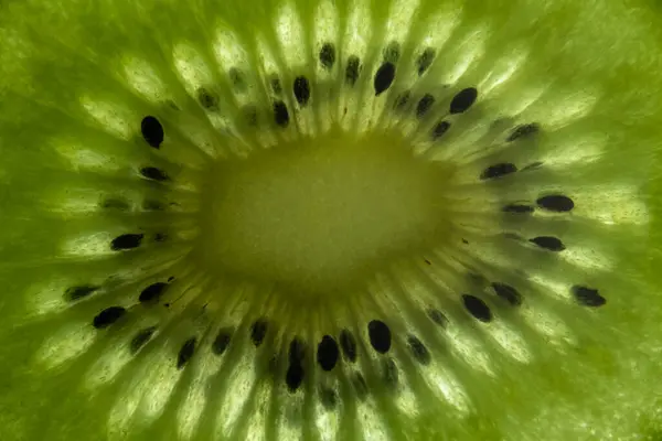 Bir kivi meyve merkezinin yakın çekim makrosu radyal tohum desenini ve sulu yeşil posasını ince detaylarıyla gösteriyor..
