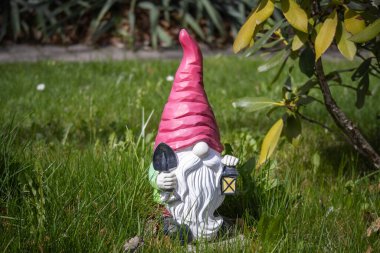 Bahçedeki yeşil çimlerin üzerinde duran pembe şapkalı ve fenerli sevimli bahçe cücesi. Açık hava bahçe tasarımı için dekoratif biblo.