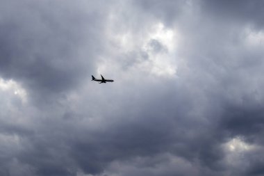 Bulutlu gökyüzünde dramatik bir ışıkla uçan uçağın silueti. Havacılık, seyahat, macera ve hava durumu için mükemmel.