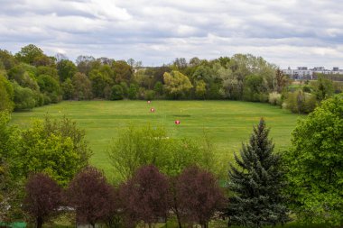 Baharda etrafı renkli ağaçlarla çevrili çimenli yeşil golf sahası. Bulutlu bir gökyüzü altında huzurlu bir açık hava, eğlence ve spor için mükemmel..