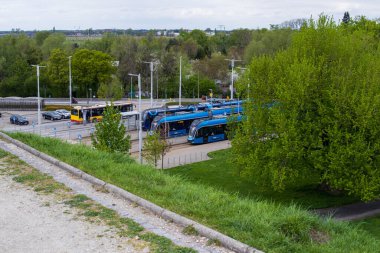 Yeşil ağaçlar ve şehir altyapısıyla çevrili şehir durağındaki modern mavi tramvaylar. Bir bahar gününde Avrupa şehrinde toplu taşıma.