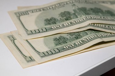 Beyaz yüzey üzerine yığılmış 100 dolarlık banknotlar, finans, zenginlik, gelir, rüşvet veya tasarrufu simgeliyor.