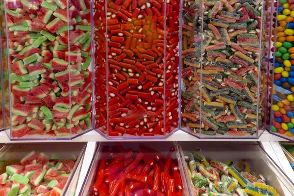 Şeffaf kaplarda renkli şeker sergileniyor. İçinde jöleli şeker, meyan kökü, ekşi şeker ve çikolata var..