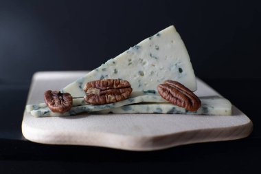 Tahtada fındıklı mavi peynir dilimi. Koyu arka planda gurme atıştırmalık kompozisyonu, aşçılık dergileri veya restoran menüleri için mükemmel..