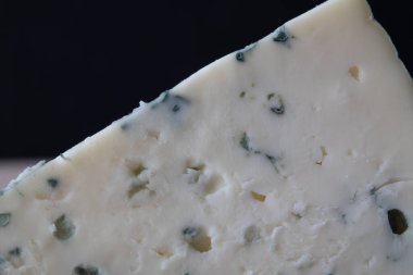 Koyu arkaplanda görünür küf damarları olan bir dilim mavi peynirin yakın çekimi. Gurme yemek temaları için zengin doku ve kremsi yüzey.