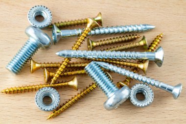 Tahta yüzeyde çeşitli metal vidalar, cıvatalar ve fındıklar var. Gümüş ve altın renginde karışık bağlayıcılar.