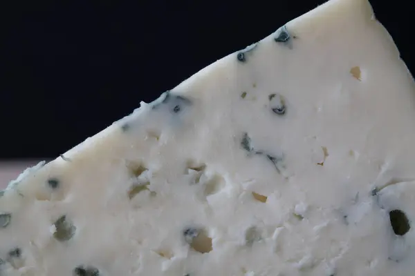 Koyu arkaplanda görünür küf damarları olan bir dilim mavi peynirin yakın çekimi. Gurme yemek temaları için zengin doku ve kremsi yüzey.