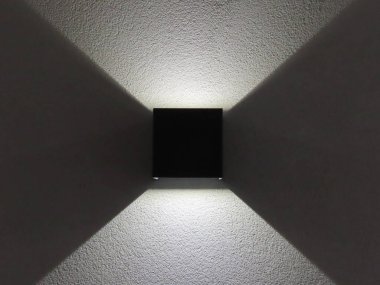 Modern siyah duvar lambası beyaz desenli bir yüzeye simetrik ışık desenleri bırakıyor. Çağdaş iç mekanlar için minimalist ışıklandırma tasarımı.