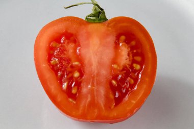 Taze olgun bir domatesin, sulu tohumlar ve iç dokuları gösteren beyaz bir arka planda ikiye bölünmüş hali..