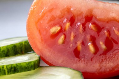 Beyaz arka planda doğranmış domates ve salatalığın makro fotoğrafı, tazeliği ve doğal dokuyu vurguluyor..