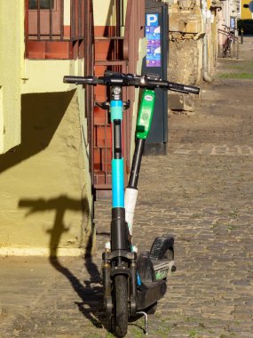 Elektrikli scooter 'lar güneşin parke taşı sokağına park edilmiş. Bina duvarına uzun gölgeler bırakıyorlar. Bir Avrupa şehir ortamında kentsel hareketlilik ve eko taşımacılık.