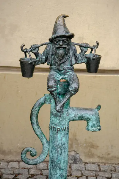 Wroclaw, Polonya 'da dekoratif bir su musluğunun üzerinde duran küçük bronz bir cüce heykelinin yakın çekimi.