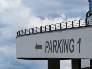 Siyah tırabzanlı ve kalın ok işaretli modern beton park yeri bulutlu gökyüzüne karşı 1 numaralı parkı gösteriyor..