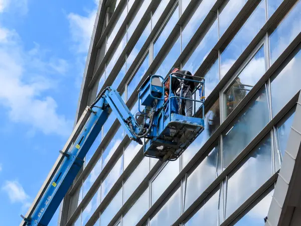 Modern bir binanın camlarını parlak mavi gökyüzüne karşı temizleyen ya da tamir eden işçilerle birlikte inşaat asansörü.
