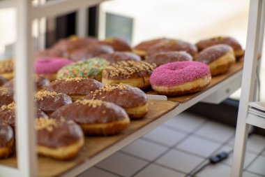 Fırındaki ahşap tepside renkli çörekler ve jöleli pastalar. Çeşitli malzemeler arasında pembe serpinti, çikolata ve fındık var..