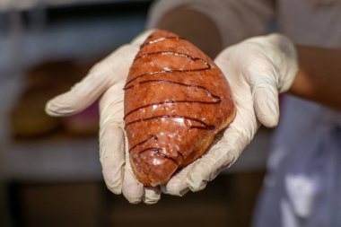 Eldivenli bir elin, çikolatalı çiselemeli, jöleli bir pastayı tutuşu. Bulanık arkaplanı olan fırın ayarı.