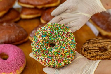 Fırında eldivenli ellerle tutulan gökkuşağı parçalı renkli donut. Tatlı pasta hazır, servis edilmeye hazır..