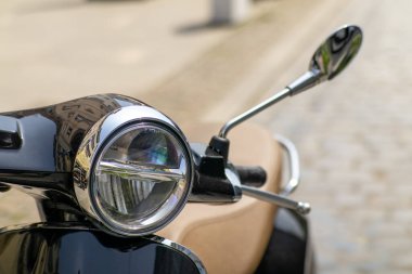 Krom farlı ve dikiz aynalı, kaldırım taşlı bir caddeye park edilmiş eski model siyah scooter 'ın yakın çekimi. Klasik şehir ulaşımı.