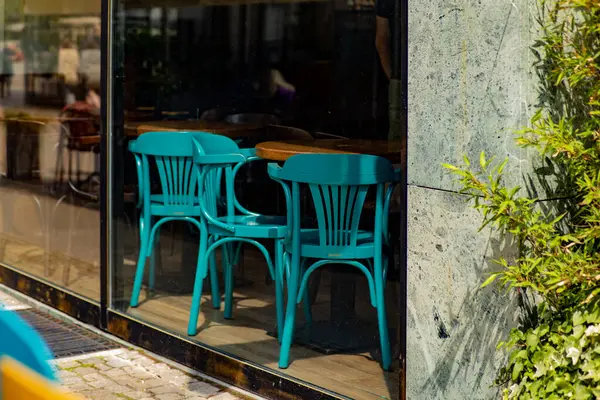 Turkuaz plastik sandalyeler ve cam bir kafenin penceresinden görülen ahşap masa modern kentsel titreşimlerle dolu açık hava koltukları..
