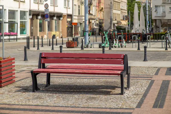 Avrupa şehir meydanında kaldırım taşı sokağındaki kırmızı ahşap bankta scooterlar ve arka planda eski binalar var. Kentsel rahatlama ve kamusal alan kavramı.