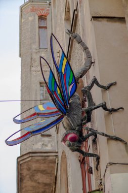 Şehir duvarına renkli cam kanatlı büyük metal böcek heykeli monte edilmiş. Kentsel sanat kurulumu Fantezi ve endüstriyel tarzı harmanlıyor.
