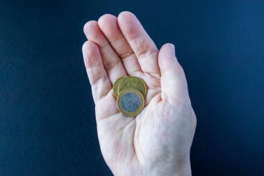 Koyu mavi arka planda Euro sikkeleri ile el ele. Avuç içinin 1 ve 2 avroluk bozukluklarının en üst görüntüsü. Günlük hayatta para, ekonomi ve finans kavramı.