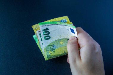 Avro banknotlarını tutan bir el koyu arka planda 100 ve 200 dolar. Avrupa Birliği 'nde finans, bankacılık, zenginlik veya tasarruf kavramı.