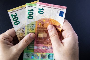 Karanlık arka planda 10, 100 ve 200 avroluk banknotları tutan eller. Avro bölgesi ülkelerinde mali zenginlik, ödeme, nakit veya tasarruf kavramı.