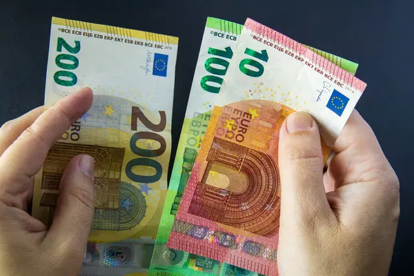 Üç avroluk banknotları tutan eller koyu arka planda 10, 100, 200 hayran şeklinde. Para, finans ve Avrupa para birimi sisteminin sembolü.